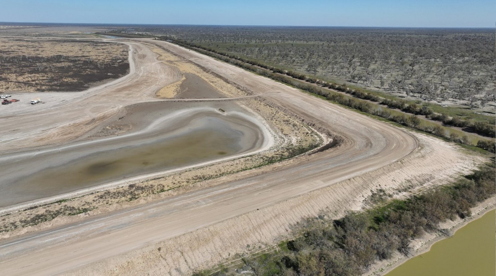 Aerial view along a mine storage cell embankment with drainage channels and a river beyond